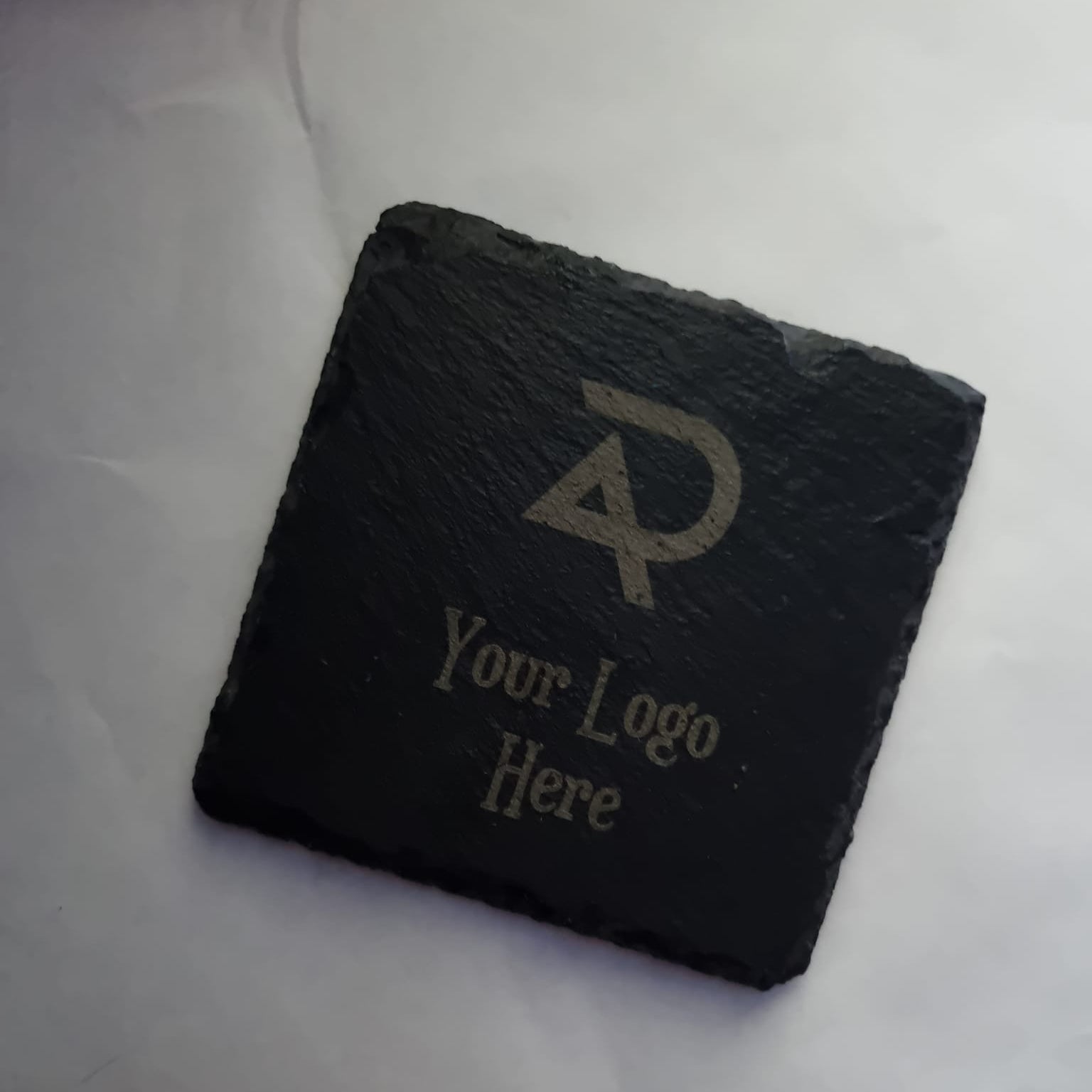 Black slate coaster with engraved logo and text on a white background