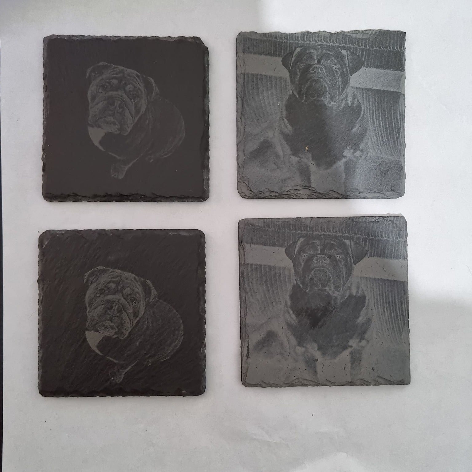 Four engraved stone coasters with dog illustrations on a white background.