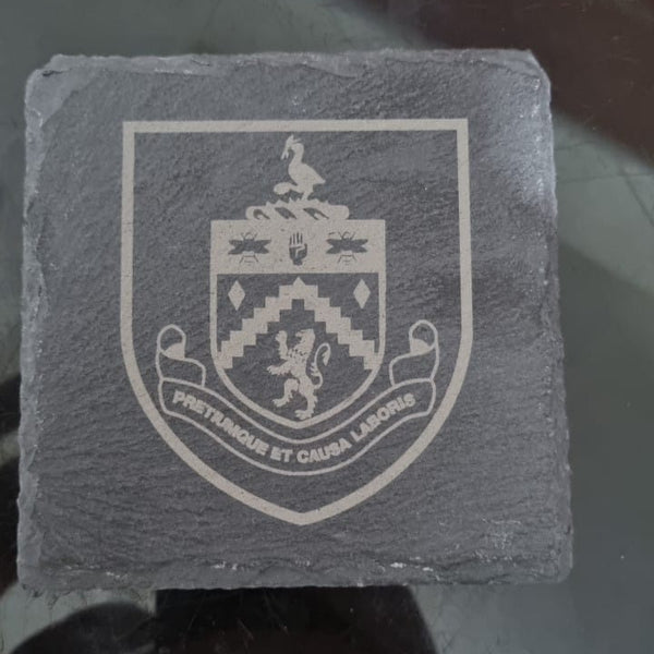 Slate coaster with engraved crest on a reflective surface